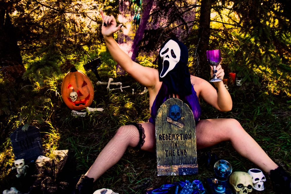 Spooky Halloween setup with jack-o-lantern, purple lighting, and decorative skulls against sunset-lit trees.