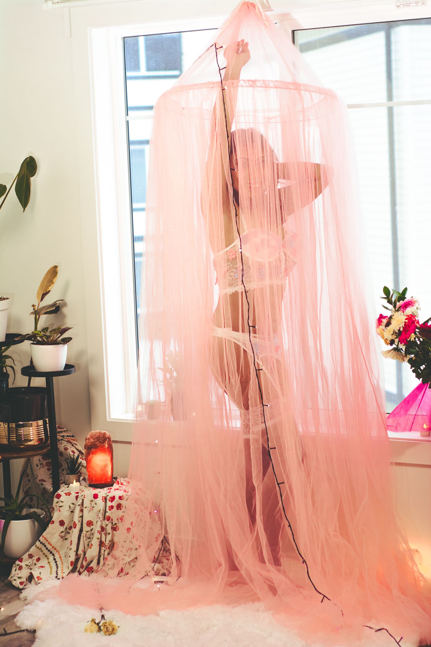 Pink translucent curtain creates a dreamy silhouette effect near a window with plants.
