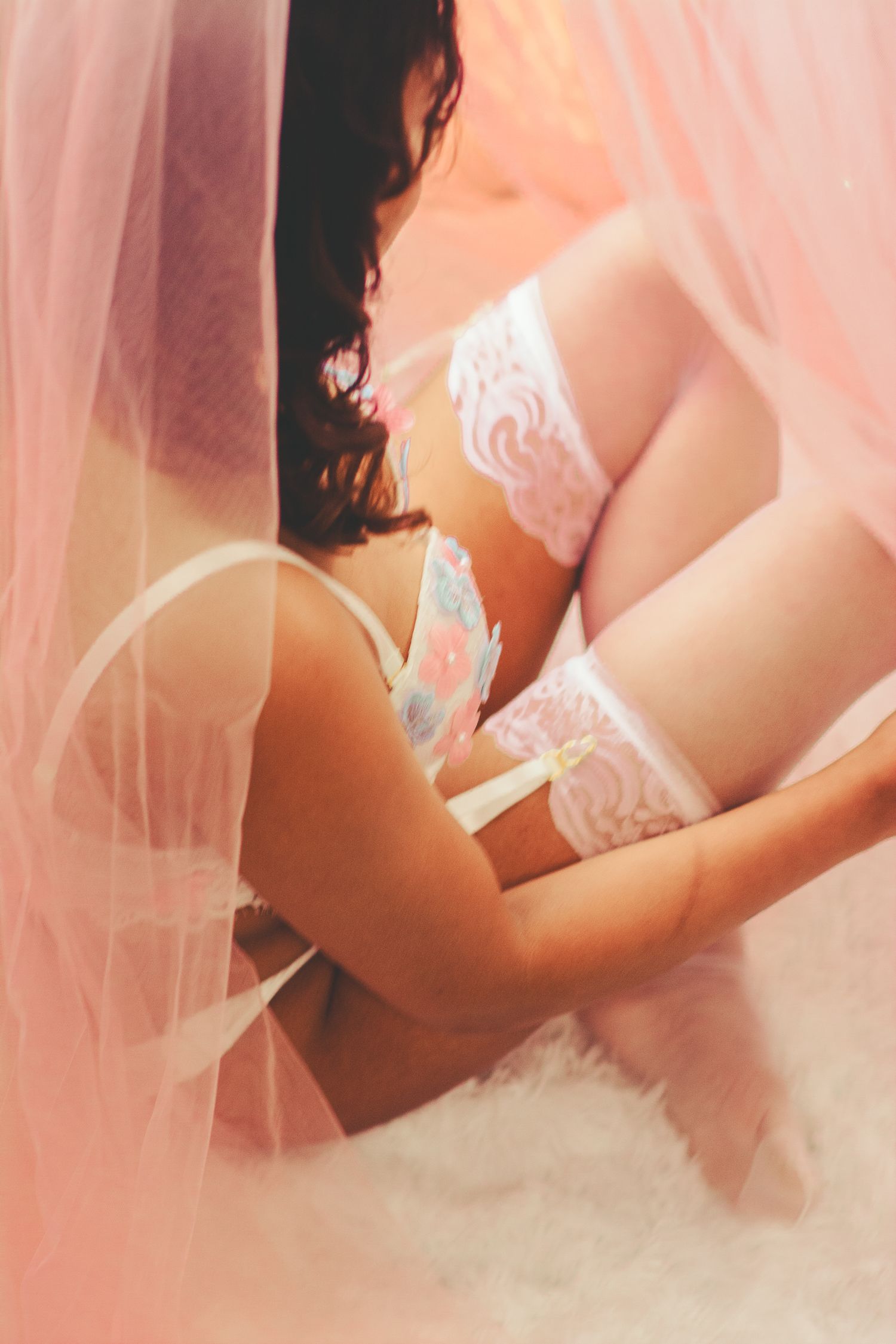 Artistic boudoir photography with pink tulle and white lace details in natural window light.