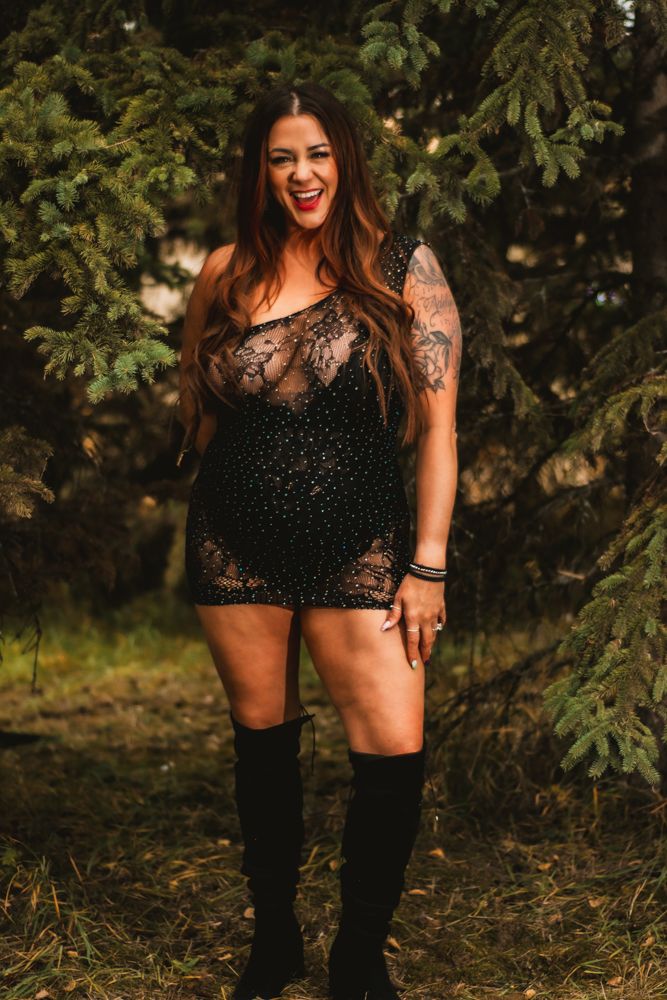 Body-positive fashion portrait in black lace outfit and knee-high boots outdoors.