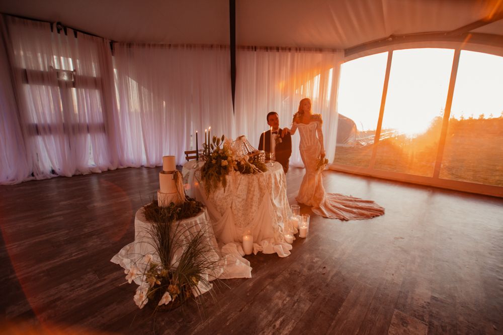Sunset wedding reception in white tent with elegant table settings and floral arrangements.
