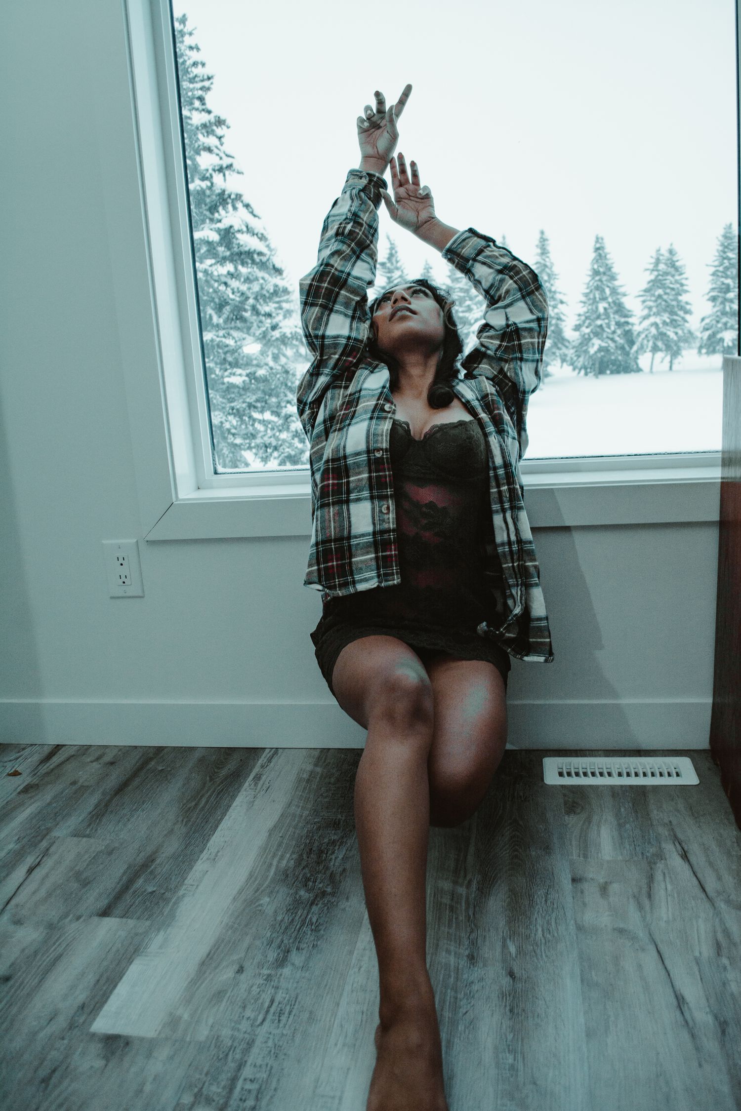 Dramatic pose on hardwood floor with winter forest visible through window.