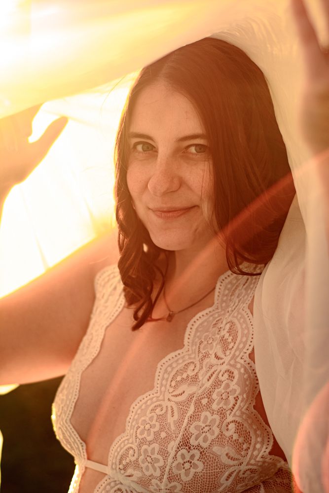 A feminine figure in white lace lingerie poses with a warm golden sunset glow in the background.