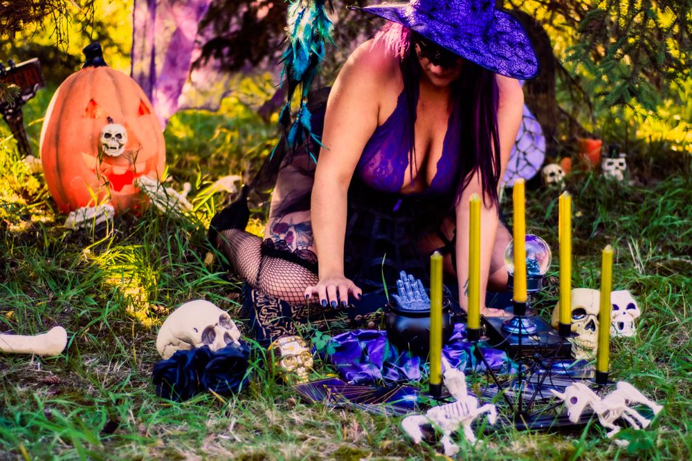 Spooky Halloween display with jack-o'-lanterns, candles, and decorative skulls in forest setting.