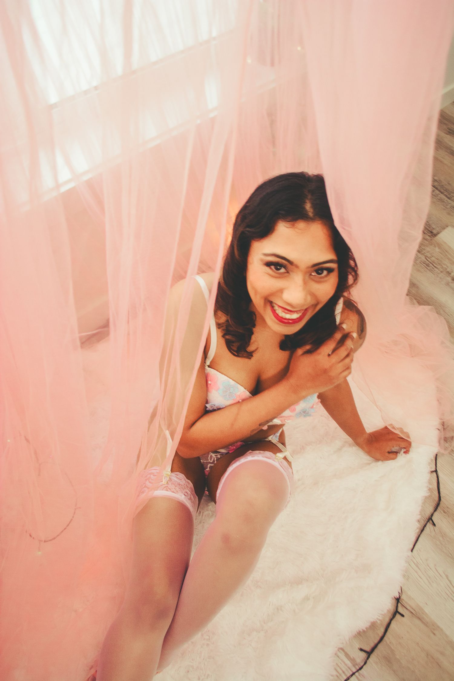 Dreamy boudoir photography with soft pink tulle draping and natural lighting.