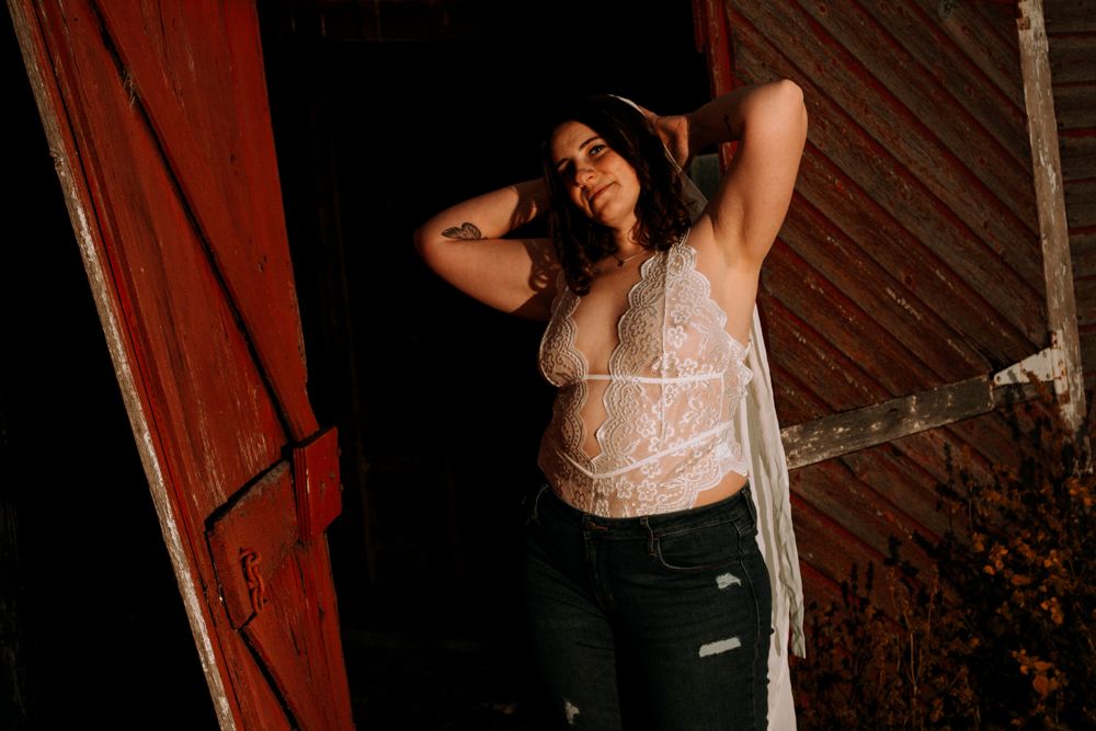 Moody portrait session inside rustic barn featuring lace bodysuit and distressed denim.