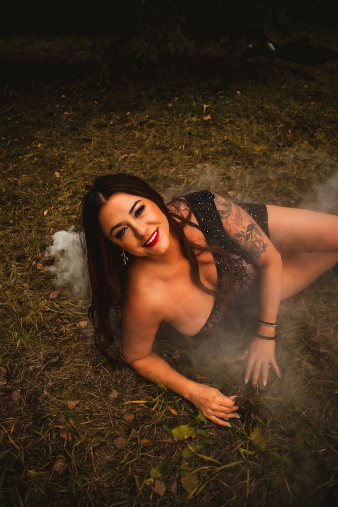 Artistic boudoir photo shoot in nature with smoke effects and black lace lingerie on autumn ground.
