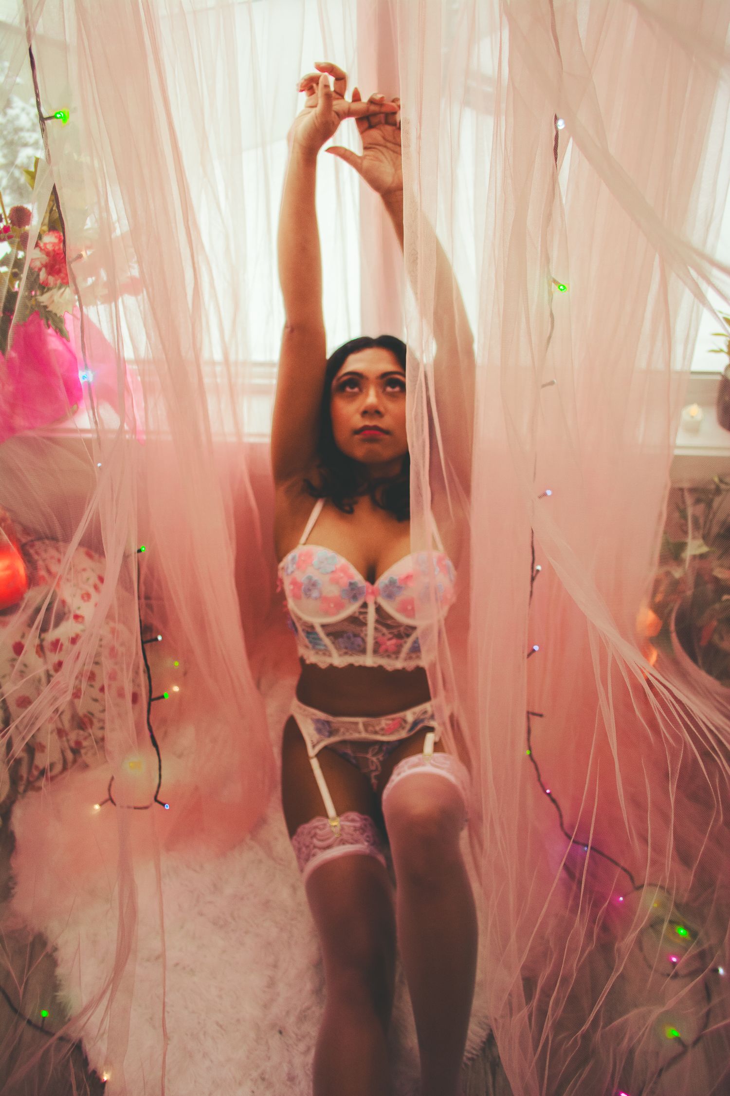 Ethereal boudoir photo with fairy lights and flowing pink fabric.