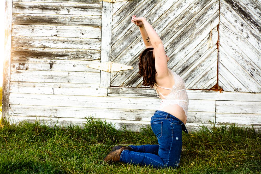 Expressive dance-like pose against weathered white barn wall in casual attire.