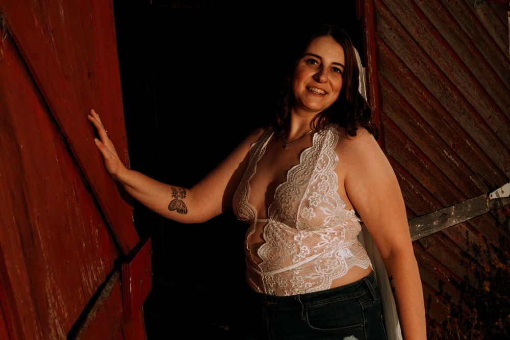 Artistic portrait against weathered red barn door showing white lace top and casual style.