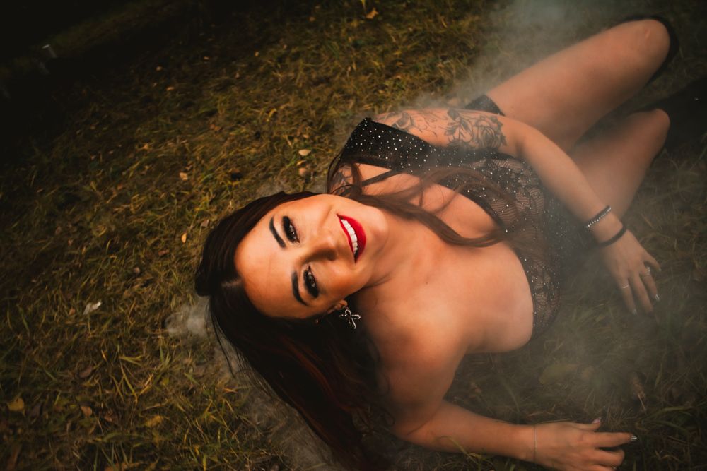 Artistic boudoir photo on grass with atmospheric smoke effects and dramatic lighting.