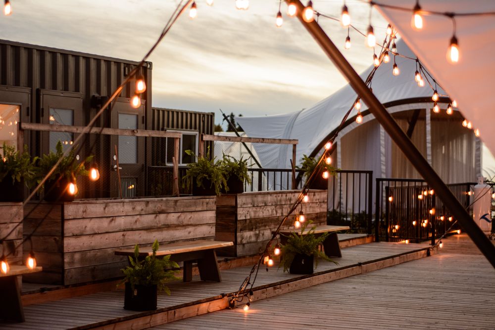 String lights illuminate a rustic outdoor deck with wooden benches at sunset.