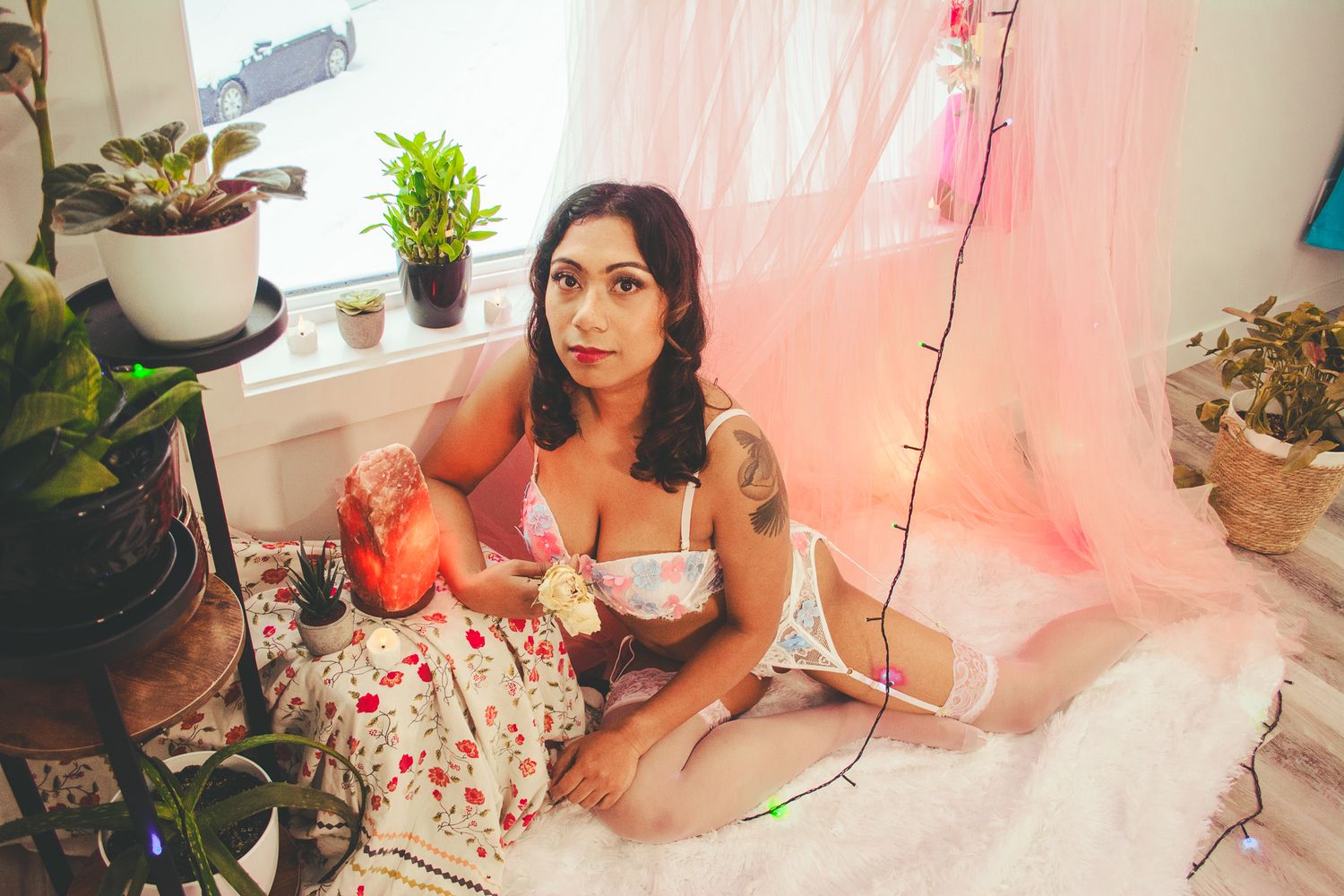 Soft natural lighting illuminates a boudoir setting with plants and pink accents.