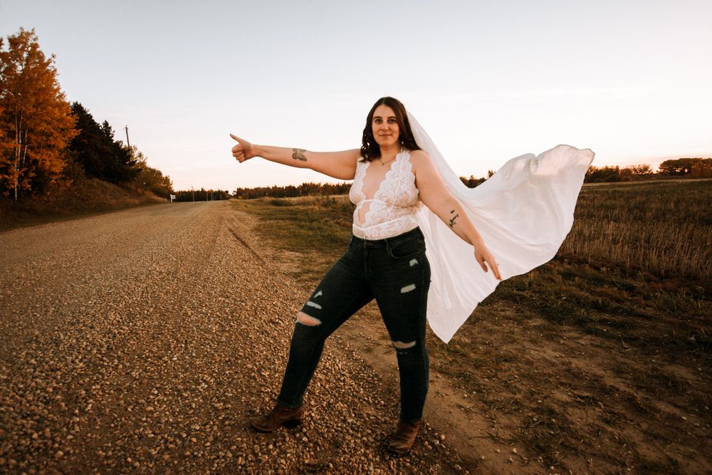 Figure with flowing white fabric striking a playful pose on country road at sunset.