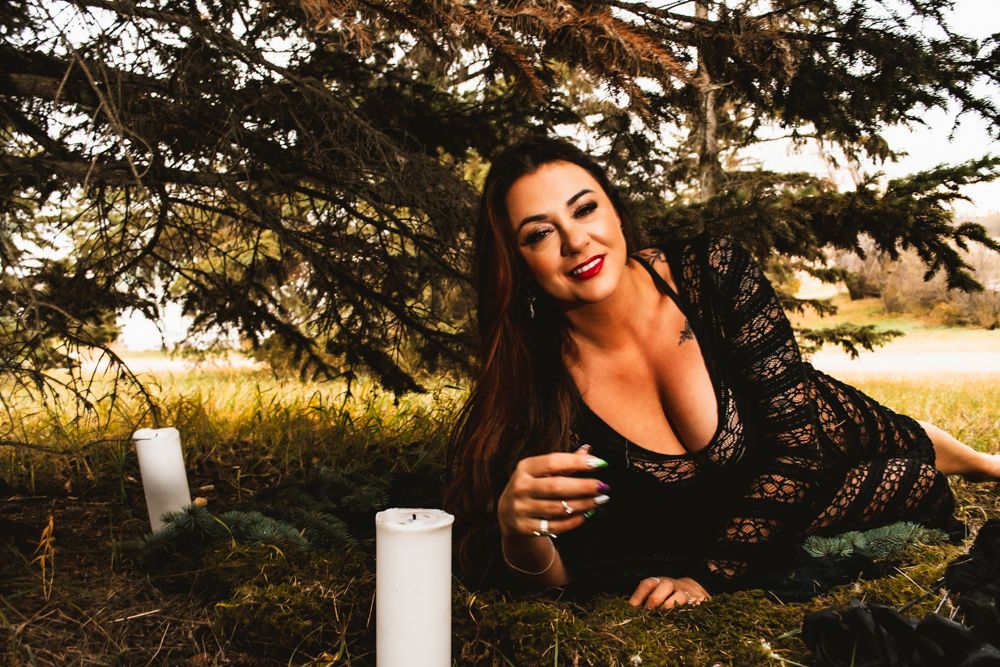 Dramatic outdoor portrait with black lace dress and white pillar candles under evergreen tree.