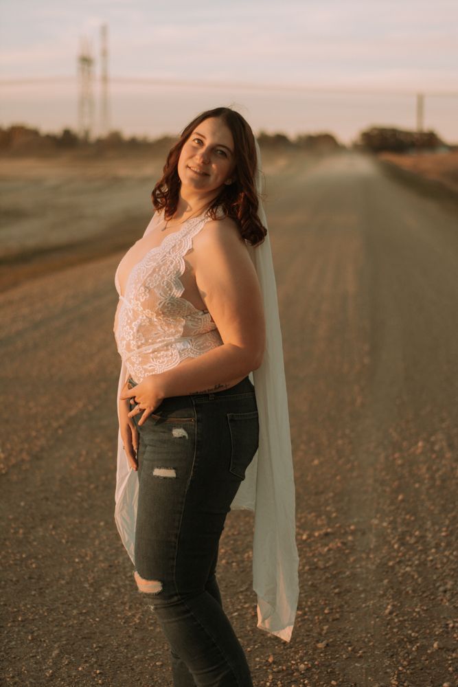 Figure in white lace top and ripped jeans stands confidently on rural road at dusk.