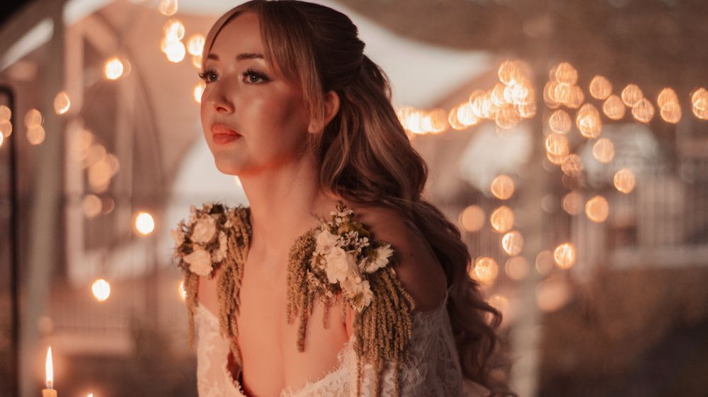 Romantic evening portrait with bokeh lights and floral shoulder decorations.
