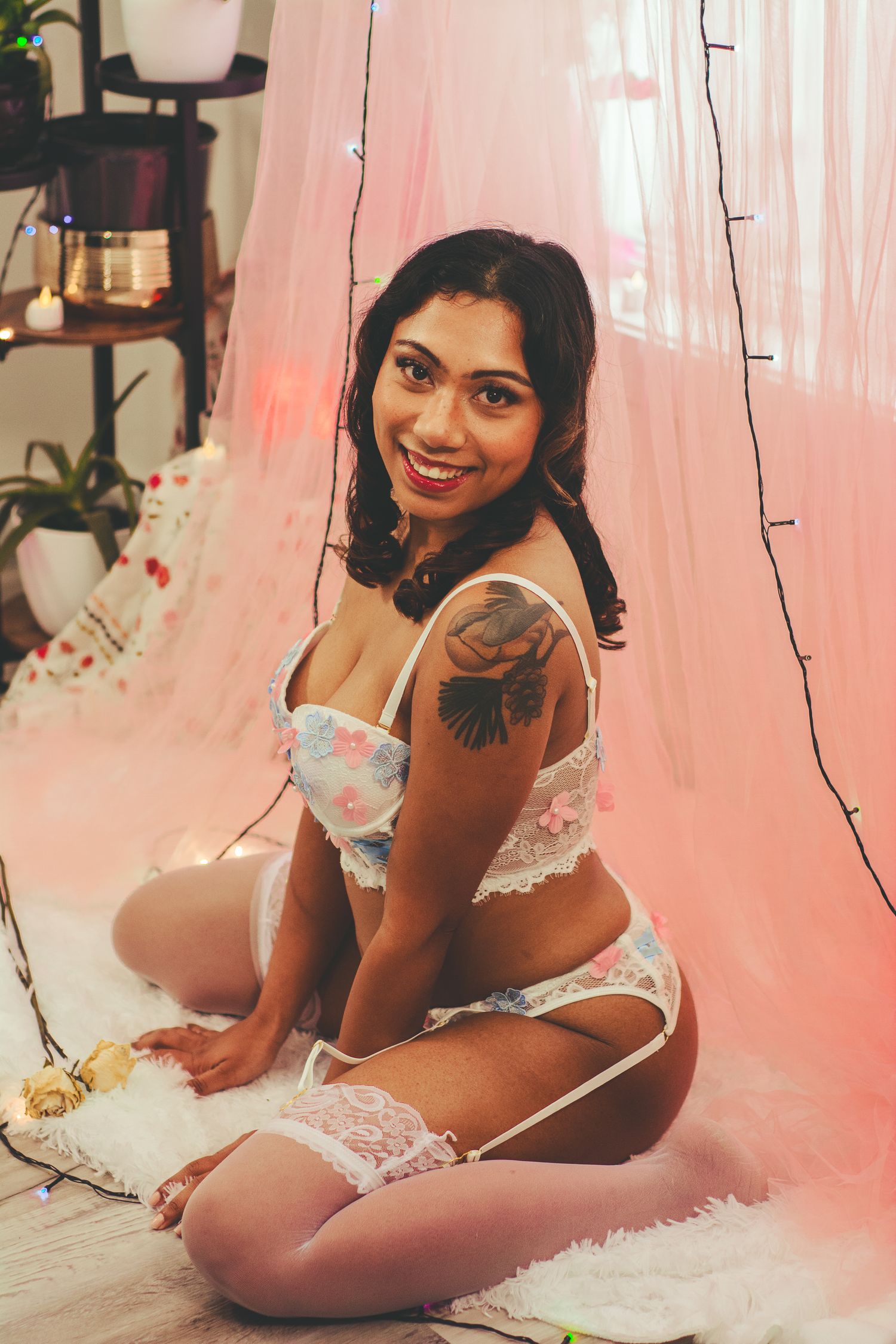 Intimate portrait with soft pink backdrop, string lights and delicate white lace lingerie details.