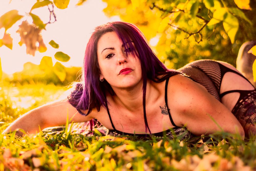 Sultry boudoir photograph with purple hair against golden autumn leaves.