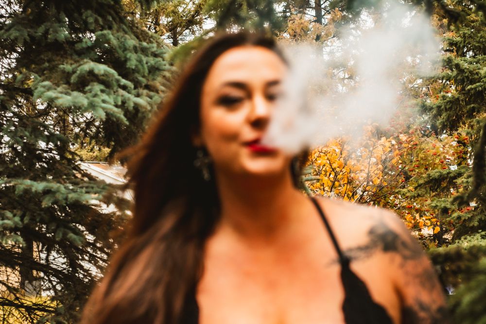 Artistic photo capturing exhaled smoke in golden autumn light with pine trees in background.