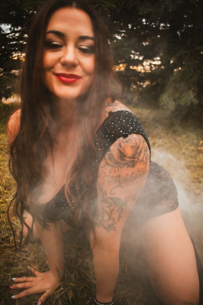 Atmospheric boudoir photo with smoke effects and natural outdoor backdrop.
