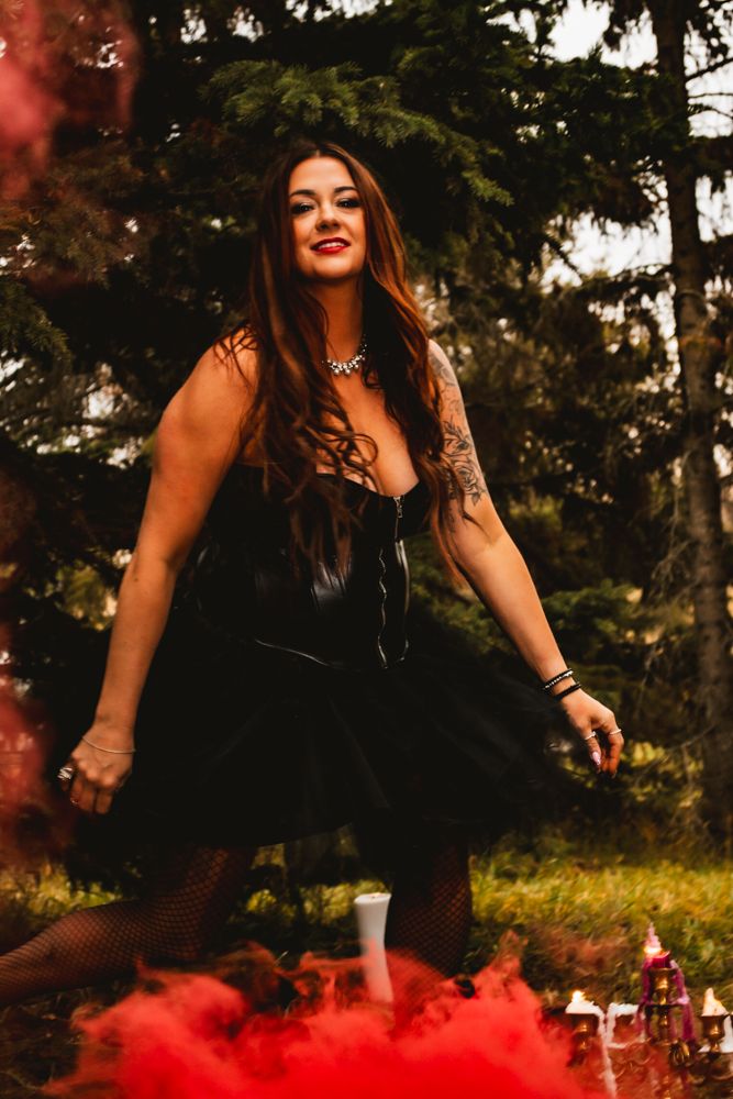 A dark fantasy photoshoot combines red smoke effects with gothic attire in a forest setting.