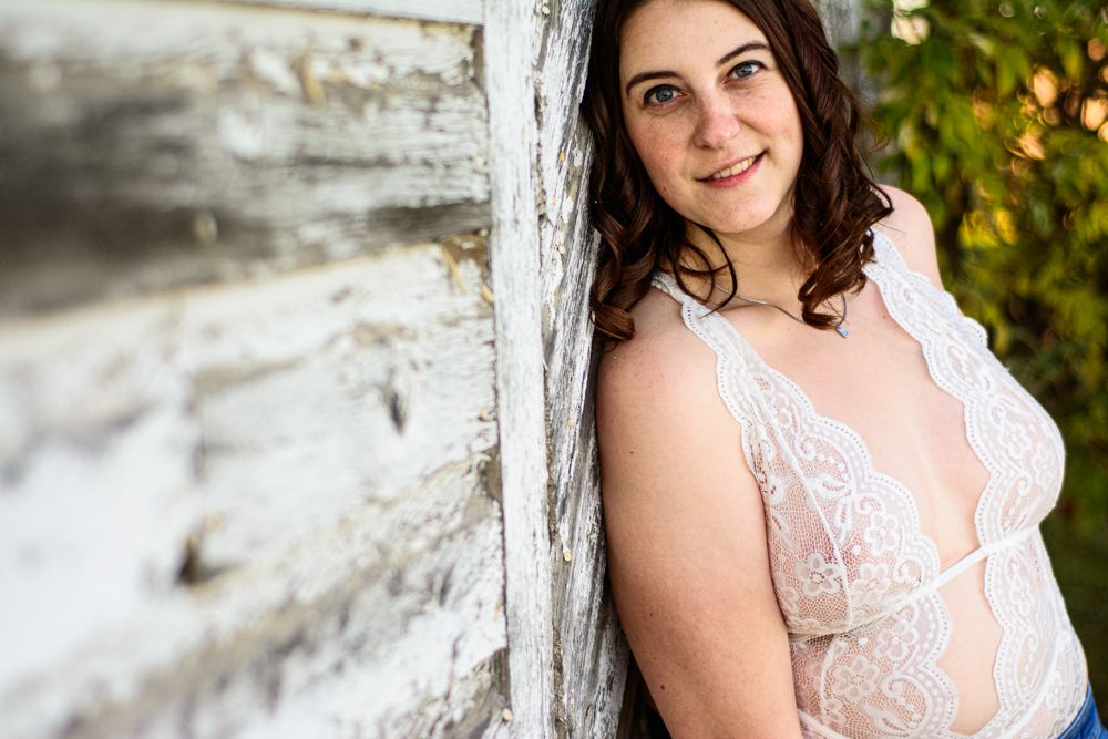 Intimate portrait leaning against rustic white wall in delicate lace top.