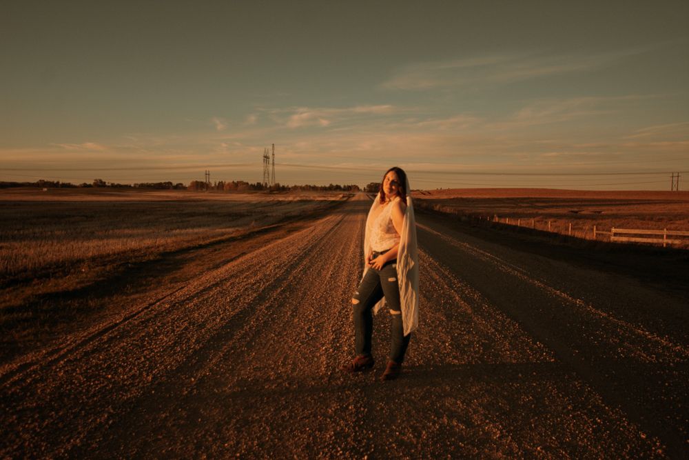 Lone figure walking on empty country road during golden sunset.