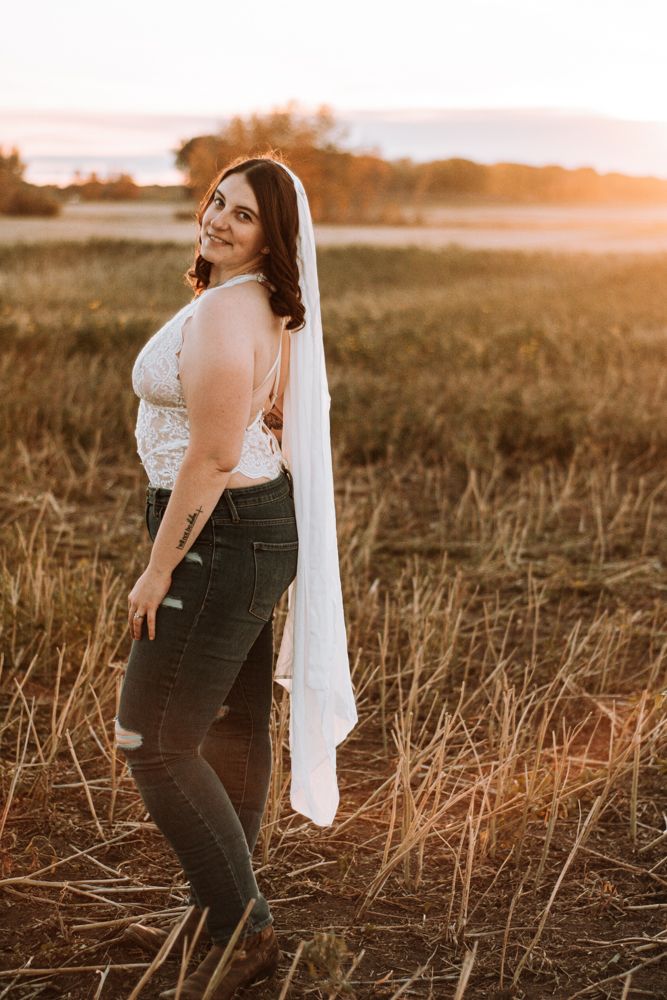 Figure wearing white lace and denim stands in golden field during sunset.