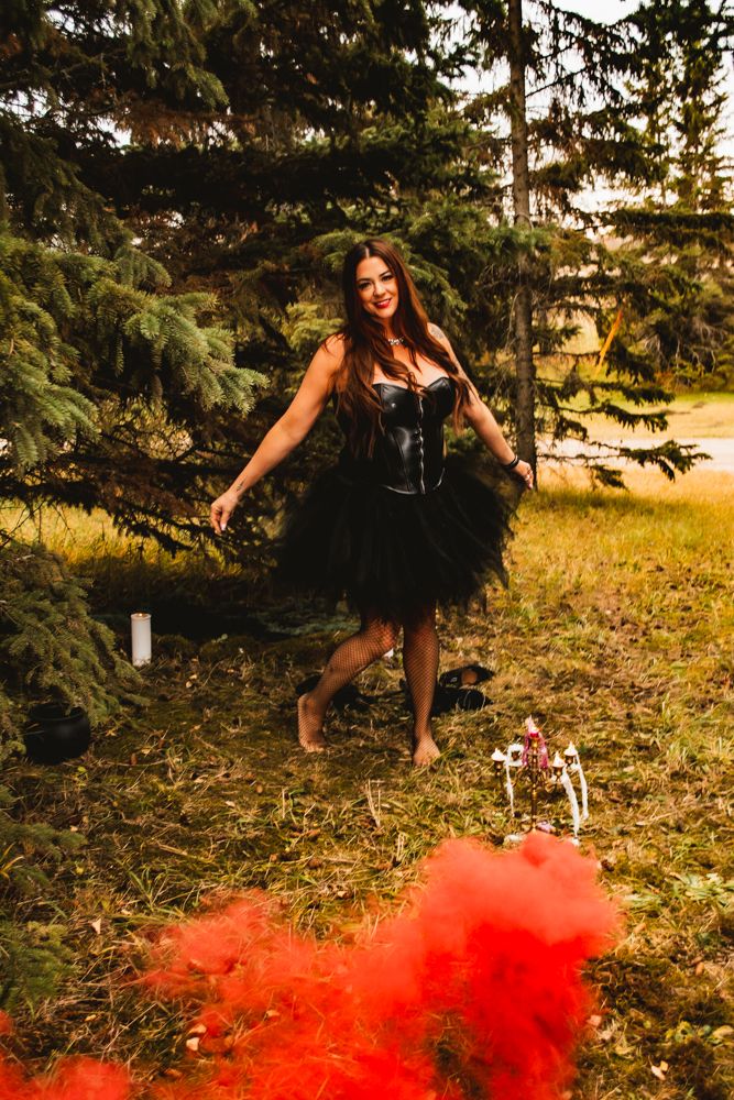 A gothic fantasy photoshoot features red smoke effects and a black tulle dress in a forest setting.