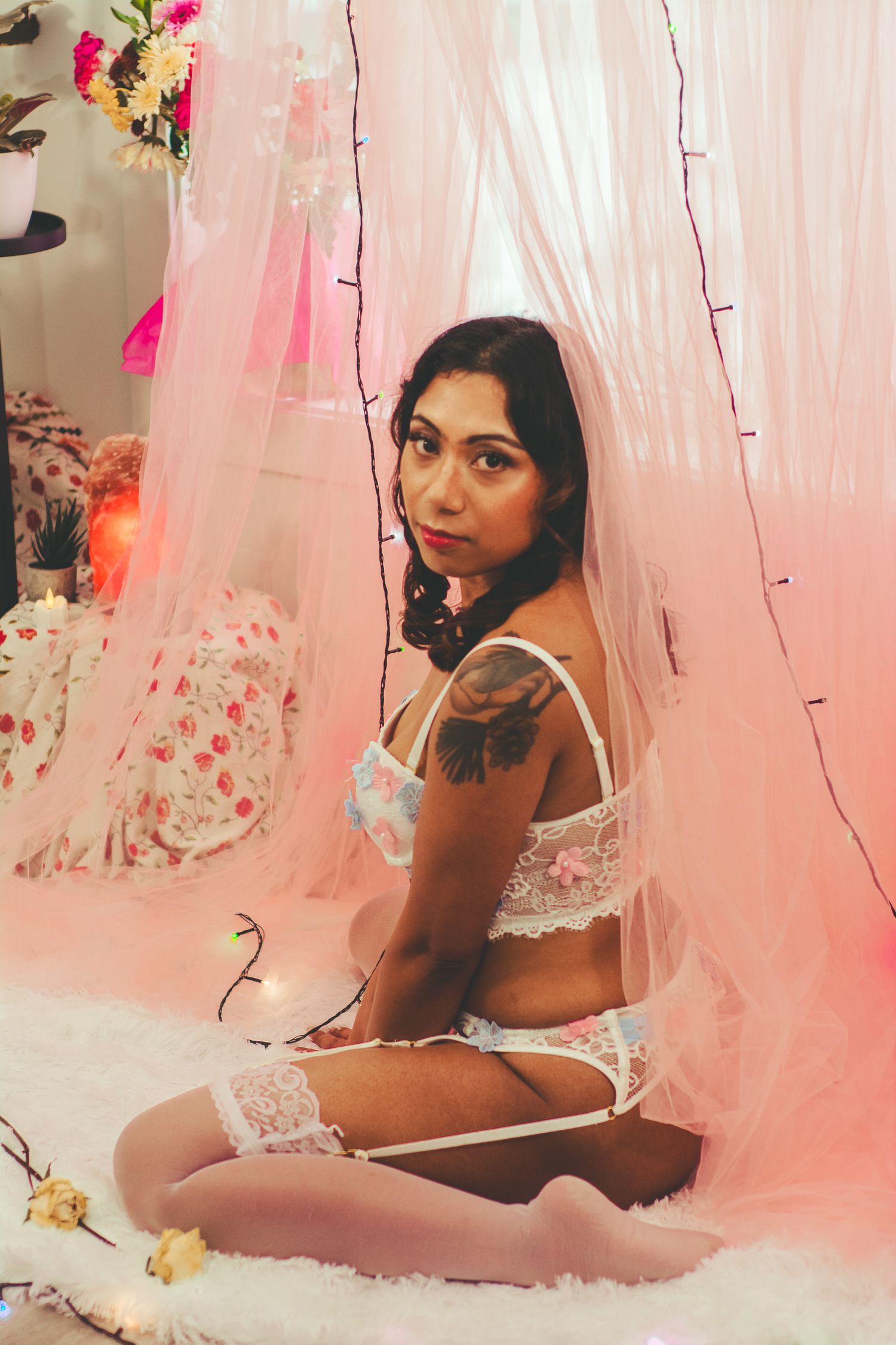 Romantic boudoir scene with pink tulle curtains, string lights and floral decorations.