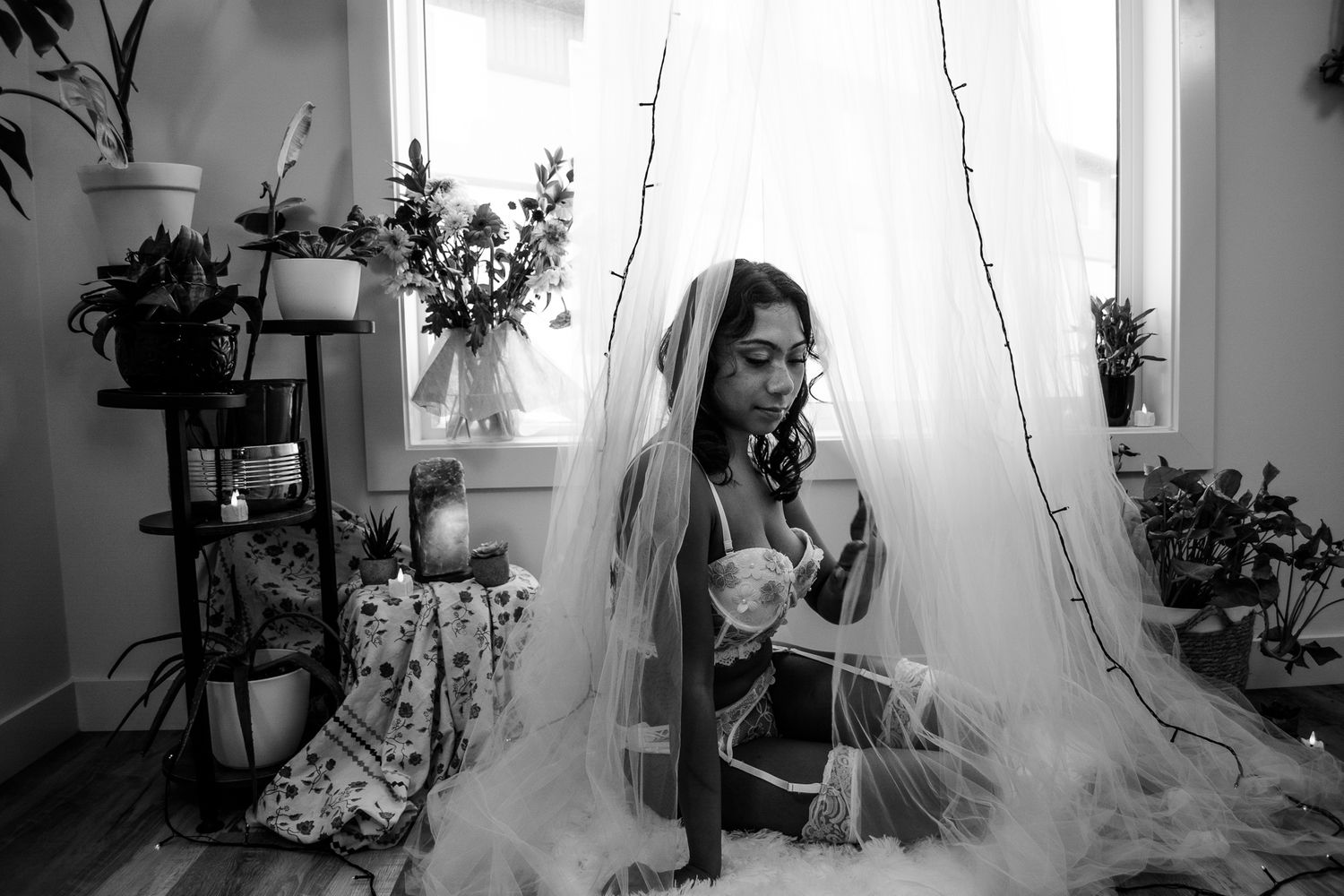 Black and white boudoir photo featuring delicate tulle draping and indoor plants.
