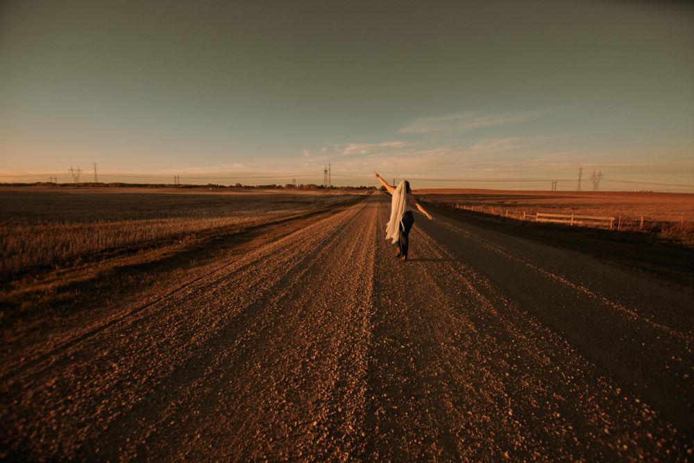 Dreamy sunset photo of person walking down empty dirt road.