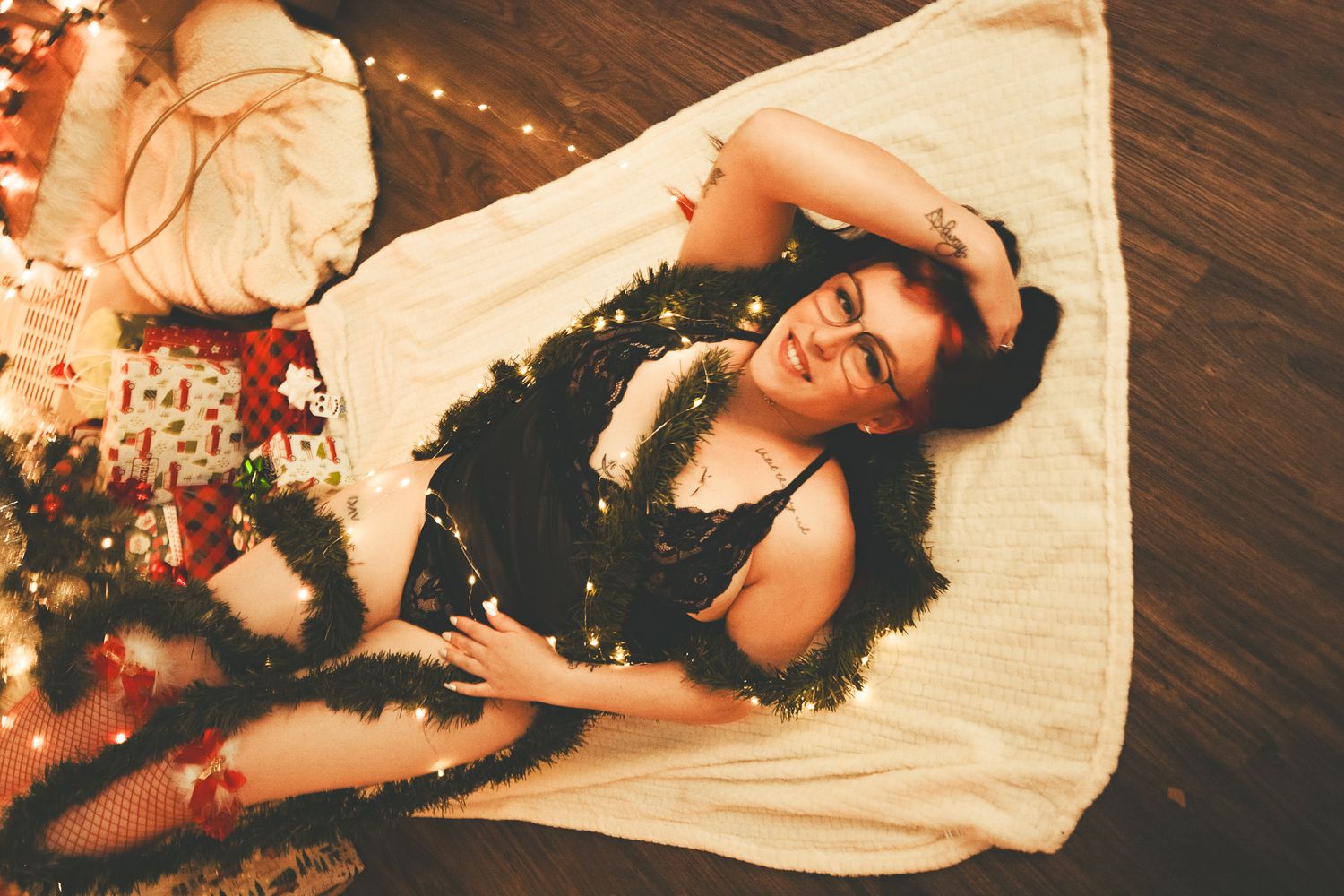 Vintage-toned holiday boudoir photo on white blanket with Christmas decor in background.
