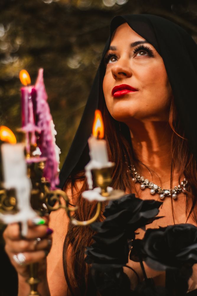 Dramatic portrait with lit candles, silver necklace, and upward gaze in forest setting.