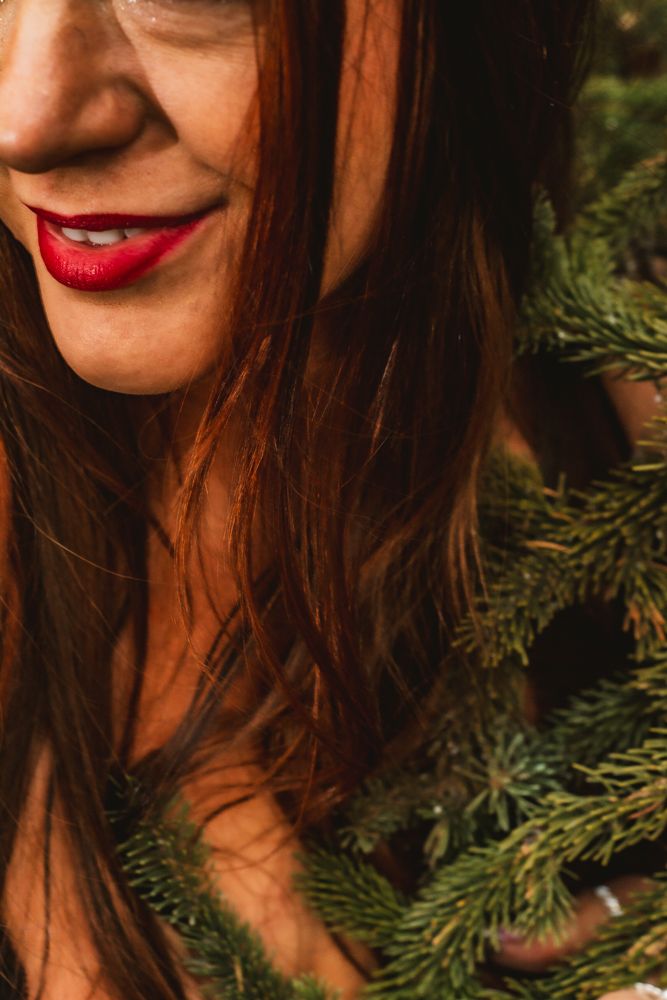 Artistic portrait with red lipstick among pine branches in warm afternoon light.
