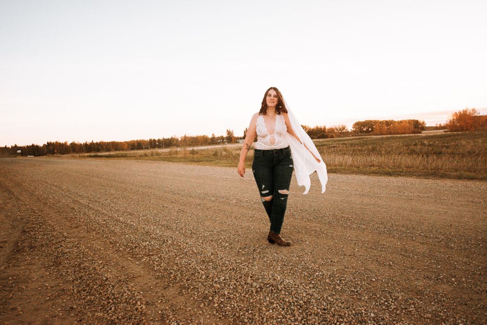Person walking on a dirt road at sunset wearing flowy white fabric and dark pants.