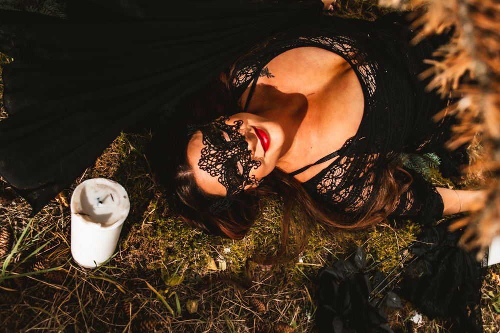 Artistic overhead shot with black lace mask and dress against natural outdoor setting.