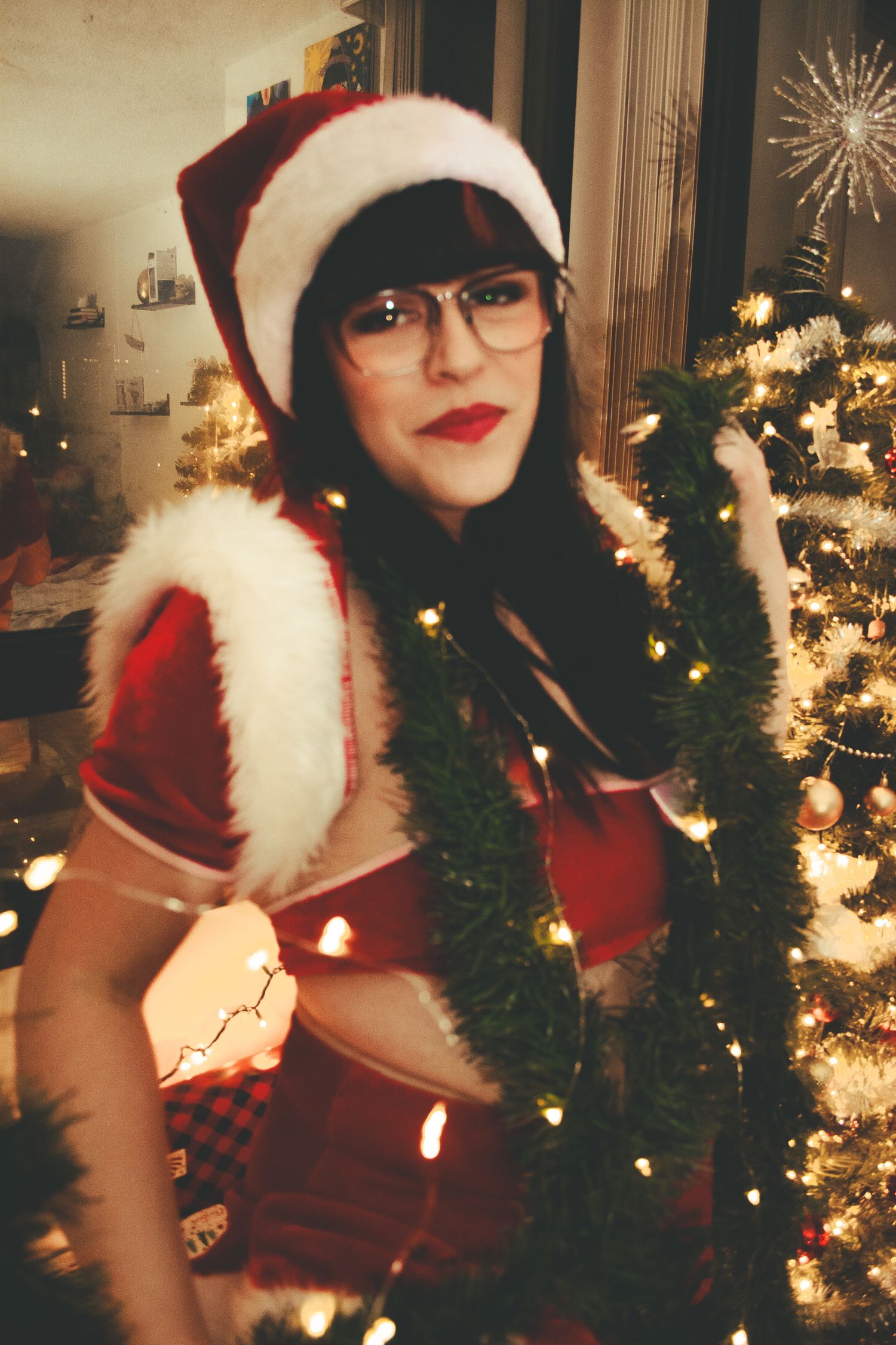 Festive holiday scene with Santa outfit and decorated Christmas tree glowing with warm lights in background.
