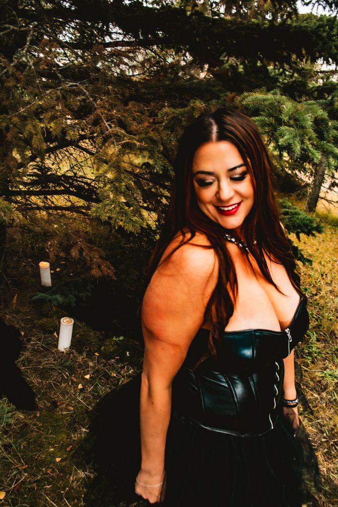 A gothic-inspired portrait against pine trees features a leather corset and dramatic styling.