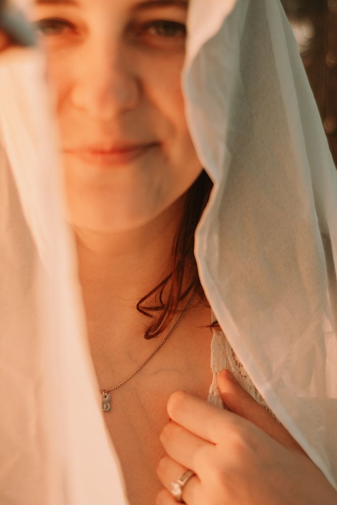 Romantic bridal detail shot with delicate veil and necklace in warm lighting.