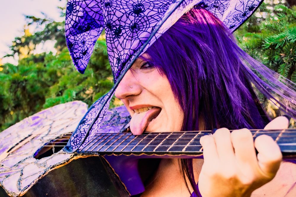 Close-up shot showing bright purple hair and playful expression while holding a decorated guitar.