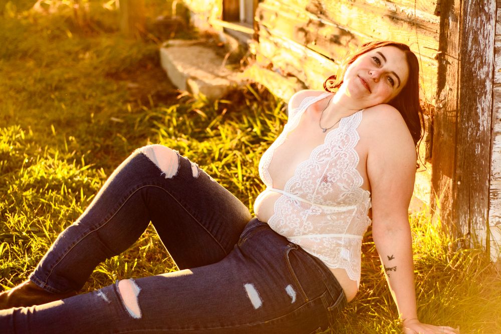 Relaxed outdoor portrait session with model lounging against rustic barn wall.