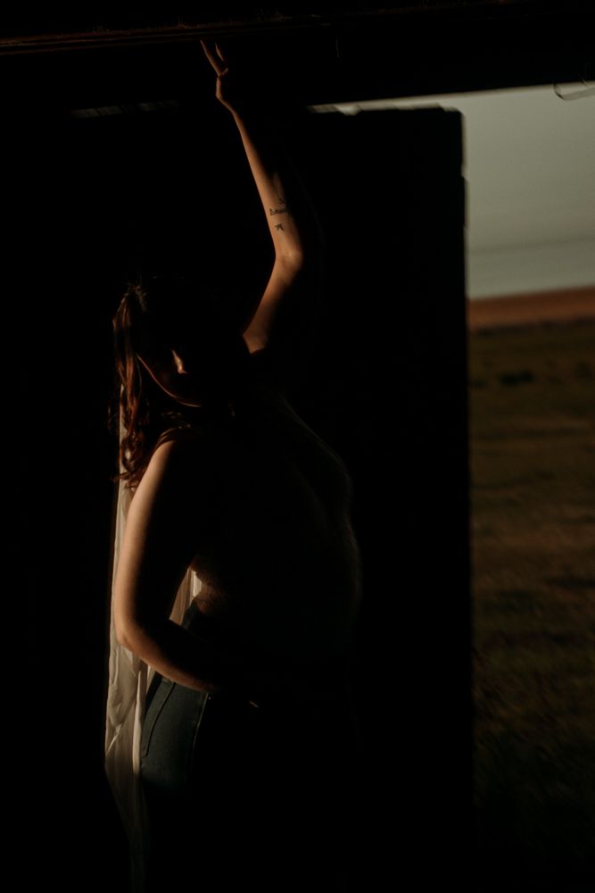 Graceful figure in flowing fabric reaching upward in shadowy doorway.