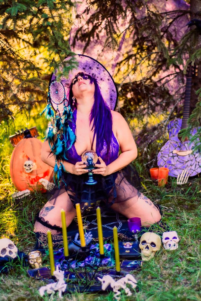 Halloween themed outdoor scene with purple decor, candles, skulls and jack-o-lanterns in a forest setting.