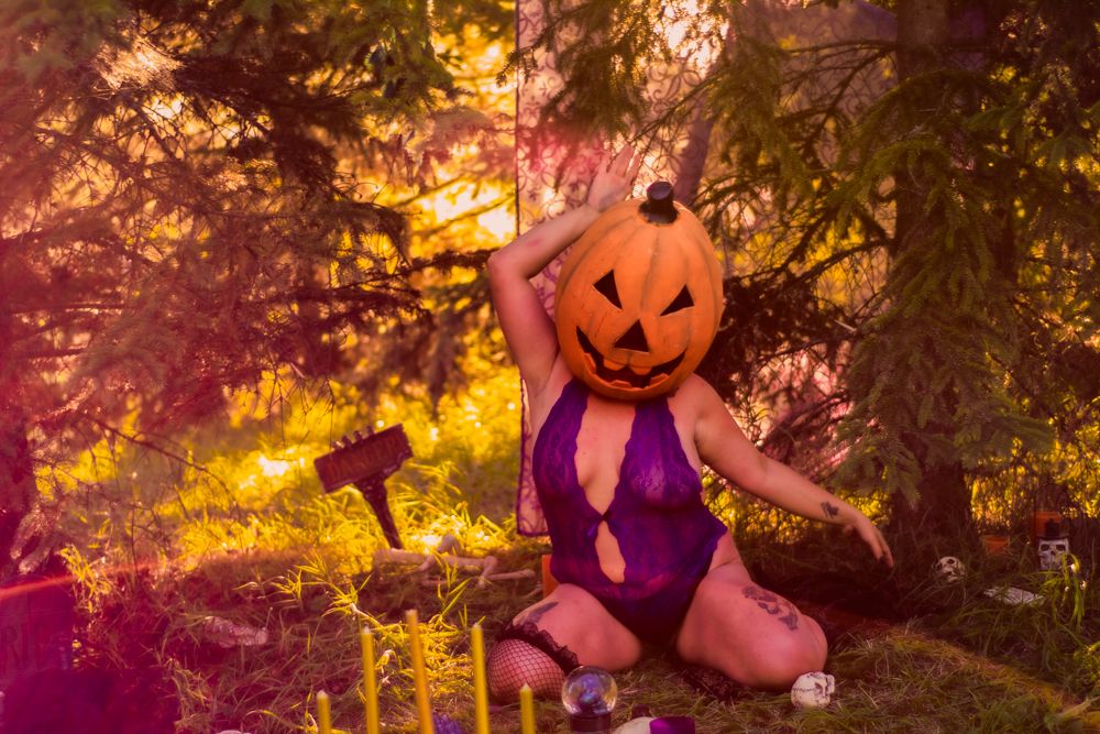 Spooky Halloween scene with pumpkin head costume and purple outfit in sunset forest setting.