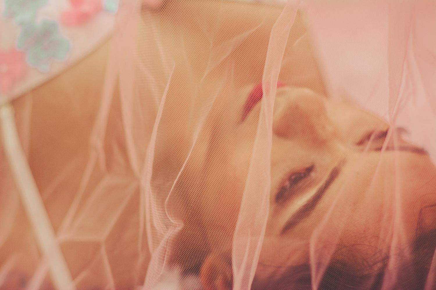 Ethereal portrait through pink sheer fabric with dreamy natural lighting.