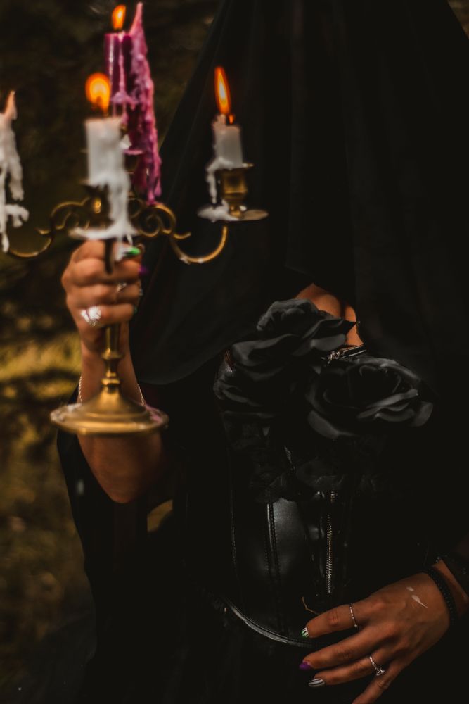 Detail shot of hands holding brass candelabra and black roses against dark fabric.