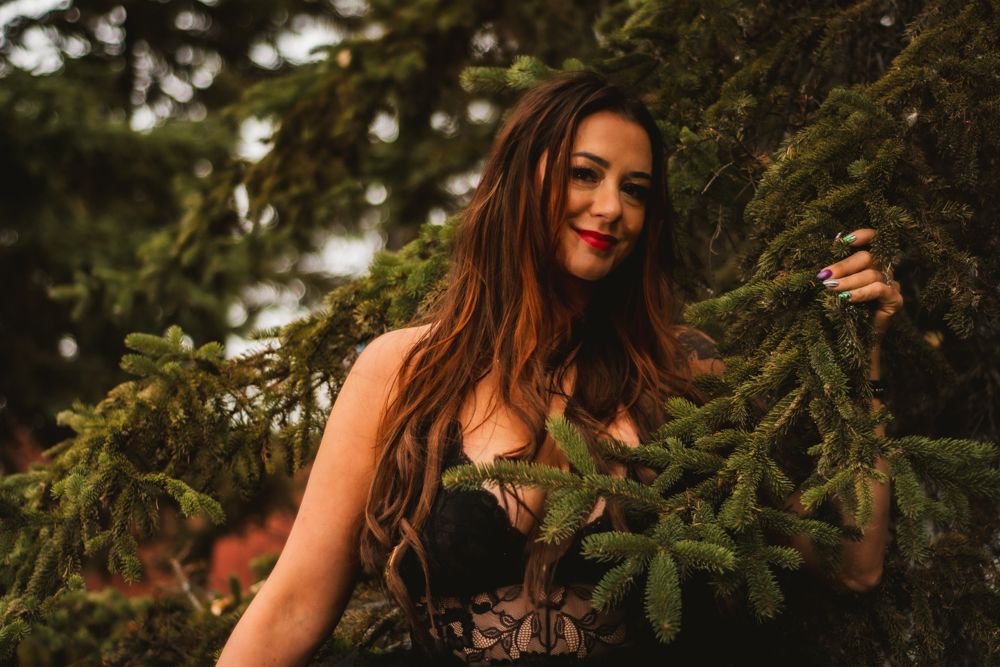 Outdoor portrait amid pine branches showing natural lighting and black lace attire.