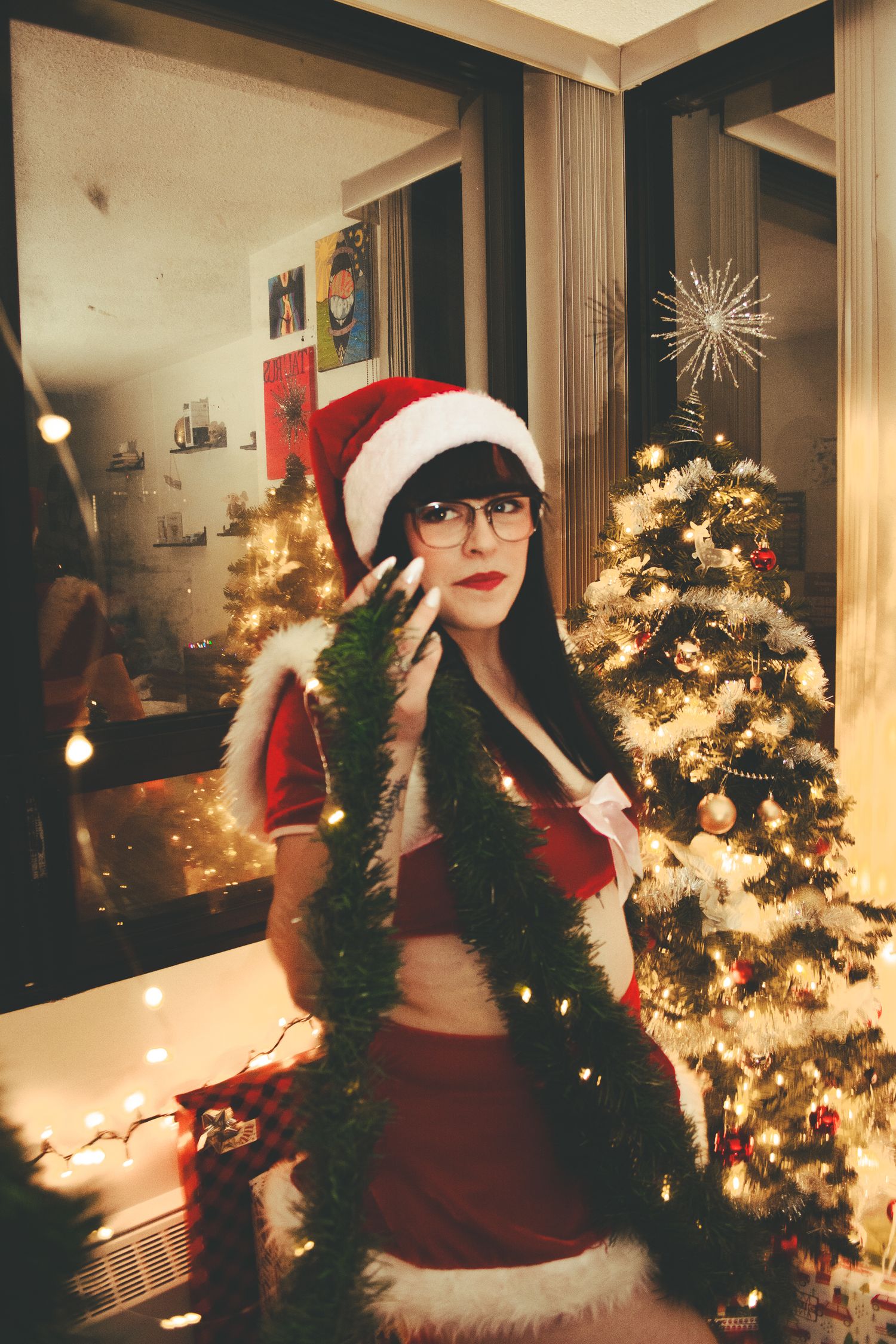 A whimsical Christmas photo with Santa hat and garland against a lit tree background.